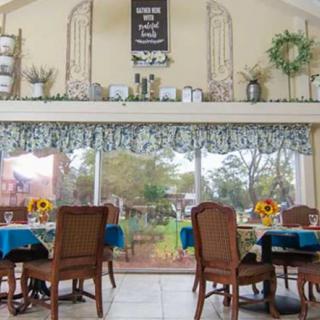 A cozy dining room with decorated tables and large windows overlooking a garden.
