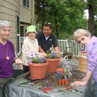 A group of people enjoying a gardening activity together outside, surrounded by potted plants and flowers.