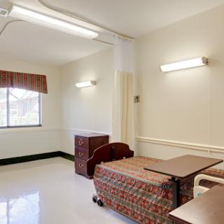 An empty hospital patient room featuring a bed, a window with curtains, and minimal furniture.