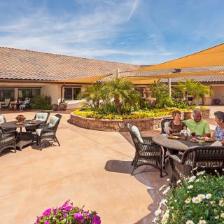 A sunny courtyard with people sitting at patio tables surrounded by lush greenery.