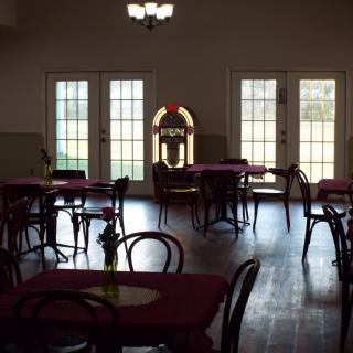 A cozy cafe interior with empty tables and chairs, featuring a jukebox against the far wall.