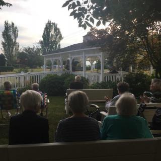 A group of seniors sitting outdoors, facing a gazebo during a social event.