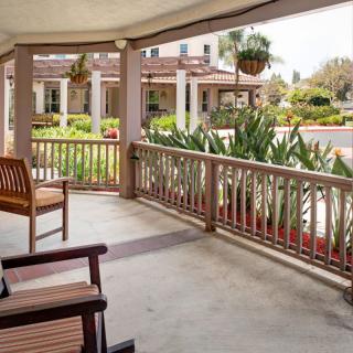 A peaceful porch with benches overlooking a landscaped garden and building.