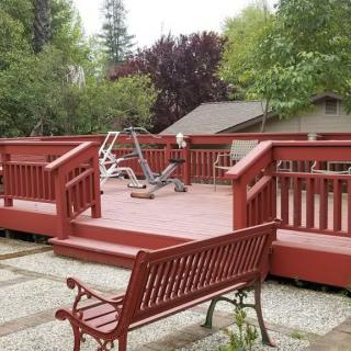 An outdoor deck with exercise equipment and a bench, surrounded by trees.