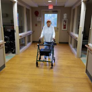 An elderly individual using a walker to navigate a healthcare facility hallway.