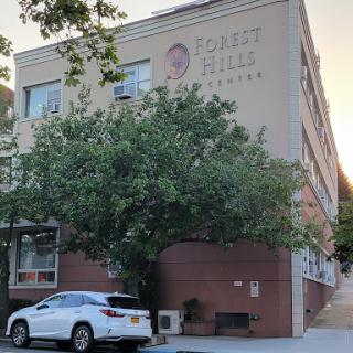 A view of a building with a tree and parked car in front.