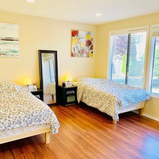A bright bedroom with two beds and wooden flooring, featuring large windows and modern decor.