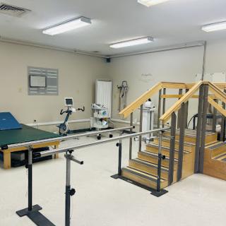 A physical therapy room equipped with parallel bars, stairs, and various exercise equipment.
