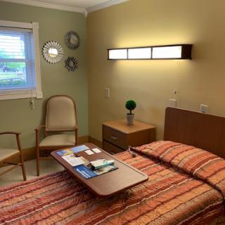 A cozy and inviting bedroom featuring a neatly made bed, a small table with books, and warm lighting.