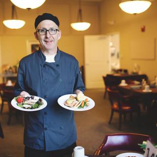 A chef presenting two plates of food in a restaurant setting.
