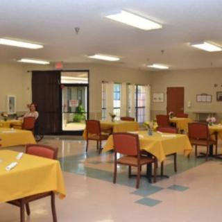 An empty dining hall with tables covered in yellow tablecloths and neatly arranged chairs.