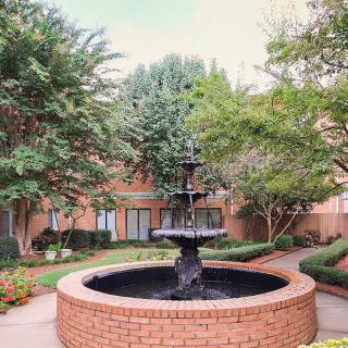 A serene courtyard featuring a multi-tiered fountain surrounded by lush greenery and brick pathways.
