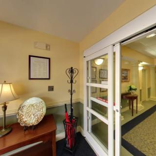A welcoming entrance area with a table, lamp, and umbrella stand near the doorway leading to a hallway.