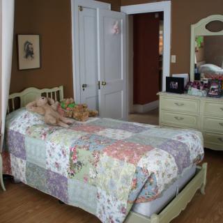 A cozy bedroom with a vintage style, featuring a bed with a patchwork quilt and a dresser with a mirror.