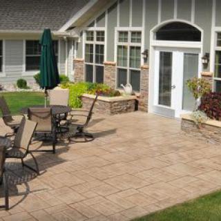 A cozy patio area with outdoor furniture and an umbrella, adjacent to a house with well-maintained landscaping.