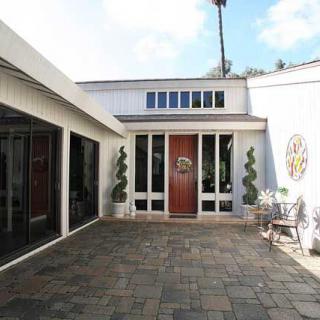 A modern courtyard entrance with large glass doors, decorative plants, and outdoor seating.