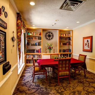 A cozy library room with a red table, surrounded by bookshelves and decorated with artwork.