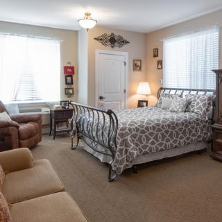 A cozy bedroom featuring a metal-framed bed, sofa, armchair, and decorative elements.