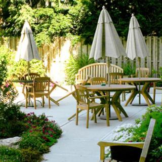 A serene outdoor patio area with wooden tables, chairs, and umbrellas surrounded by greenery.