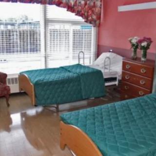 A healthcare room with two patient beds, a dresser, and a window with curtains.