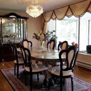 A classic dining room with a chandelier, a large dining table surrounded by chairs, and a window adorned with elegant curtains.