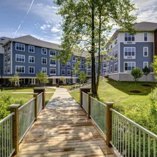 A picturesque scene of a modern apartment complex with a wooden bridge and lush greenery.