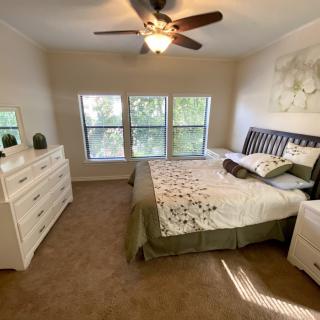 A cozy bedroom with a large bed, dresser, and ceiling fan, featuring a window with natural light.