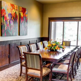 A bright dining room with a large table and chairs, decorated with colorful artwork and a floral centerpiece.