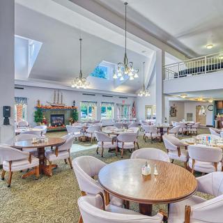 A spacious dining area with multiple tables and chairs, featuring chandeliers and a carpeted floor.