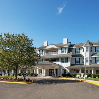 A large residential building with a circular driveway and landscaped surroundings on a clear day.