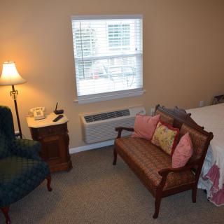 A cozy bedroom with a chair, small sofa, and bedside lamp.