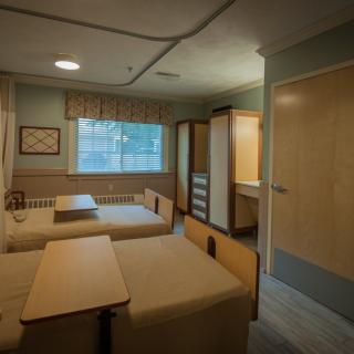 A hospital room with multiple beds and natural lighting.