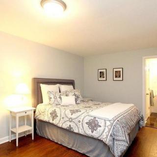 A cozy bedroom with a neatly made bed, white nightstand, and soft lighting.