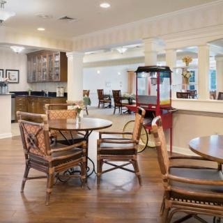 A cozy seating area with wooden tables and chairs, featuring a popcorn machine and kitchen in the background.