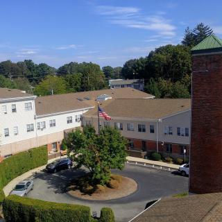 Aerial view of a residential area with buildings, a parking lot, and a flagpole surrounded by trees.