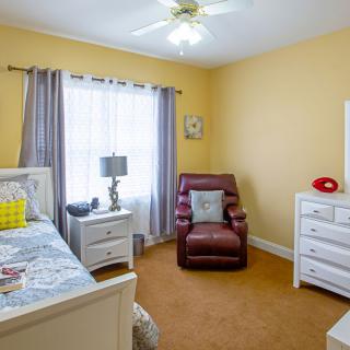 A cozy bedroom with yellow walls, featuring a comfortable armchair, a bed, and a window with curtains.