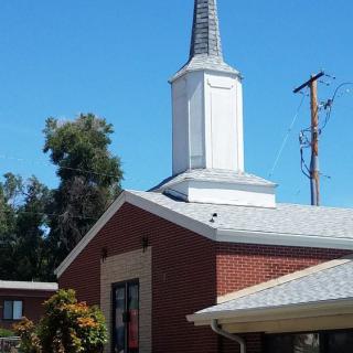 A brick church with a white steeple under a clear blue sky.