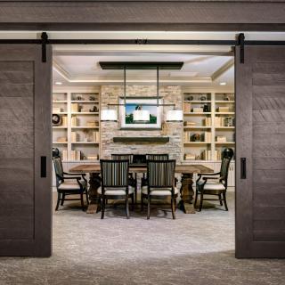 A modern conference room with sliding doors, featuring a central table surrounded by chairs, bookshelves along the walls, and a TV screen mounted above.