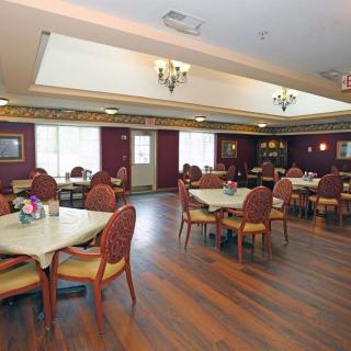 A spacious dining area with neatly arranged tables and chairs, featuring elegant ceiling lights and a warm wooden floor.