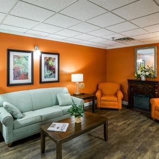 A cozy living room with orange walls, featuring a light blue sofa and matching armchairs, a wooden coffee table, and decorative artwork.