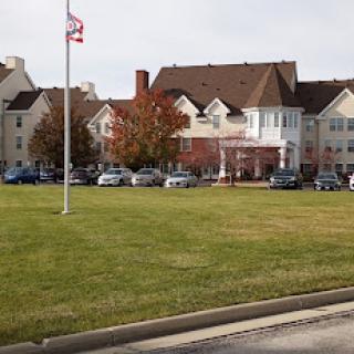 A hotel building surrounded by grass and a flag, with vehicles parked out front during autumn.