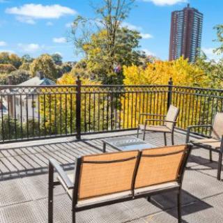 A rooftop terrace with outdoor furniture overlooking autumn trees and a city skyline.