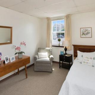 A cozy bedroom with a comfortable chair, bed, and wooden furniture in a well-lit space.