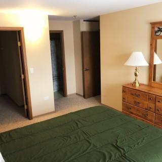 A cozy bedroom featuring a bed with a green blanket, wooden dresser with a mirror, and a lamp.