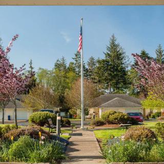 A well-maintained garden with a flagpole, surrounded by blooming trees and houses.