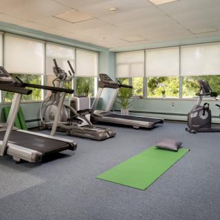 A well-lit gym with treadmills, a stationary bike, and a yoga mat.