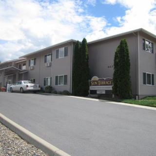 An apartment building with a parking lot and trees under a cloudy sky.