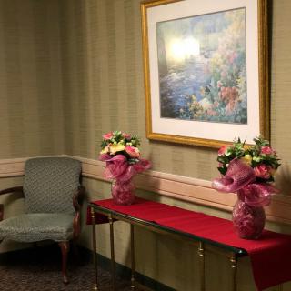 A decorated room corner featuring two floral bouquets on a table beneath a framed painting.