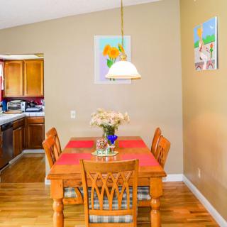 A cozy dining area with a wooden table set for four, featuring a flower vase centerpiece, adjacent to a kitchen.