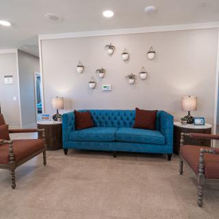 A stylish living room with a blue sofa, two brown chairs, and modern wall art.